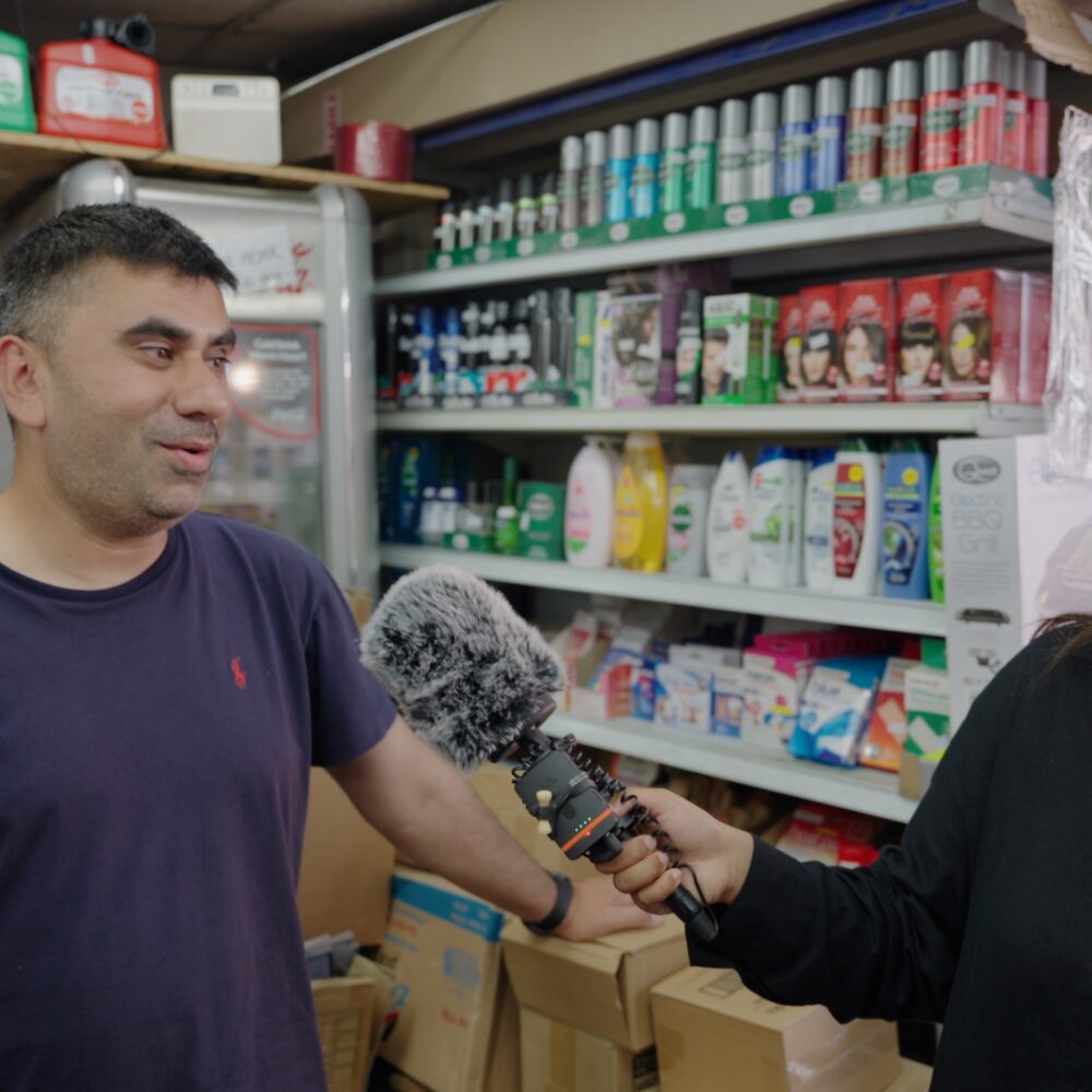 Interviewer with microphone speaking to Luton shop owner