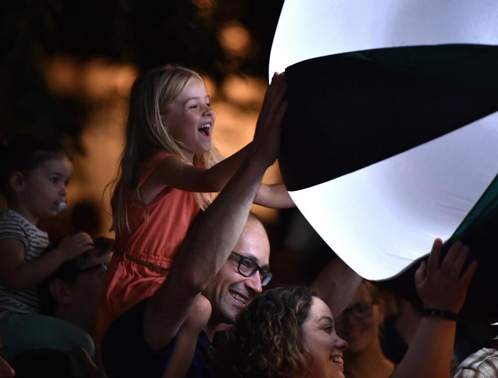 Young girl sits on a man's shoulders to touch an illuminated ball